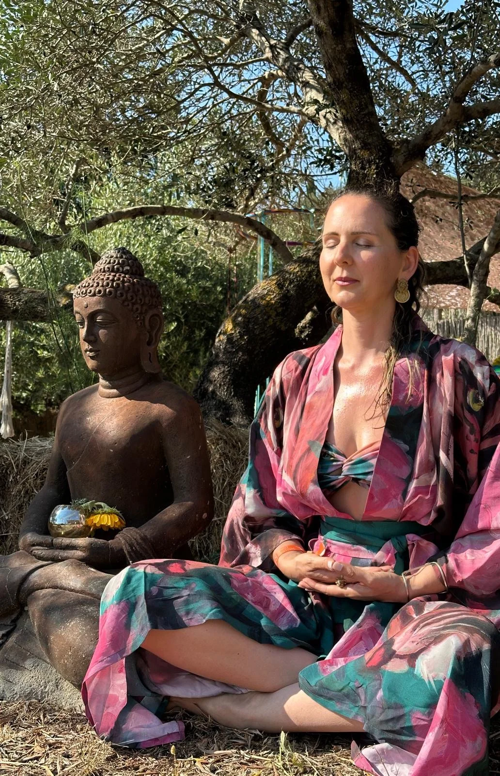 Loukia Papa in meditation beside a Buddha beneath an olive tree