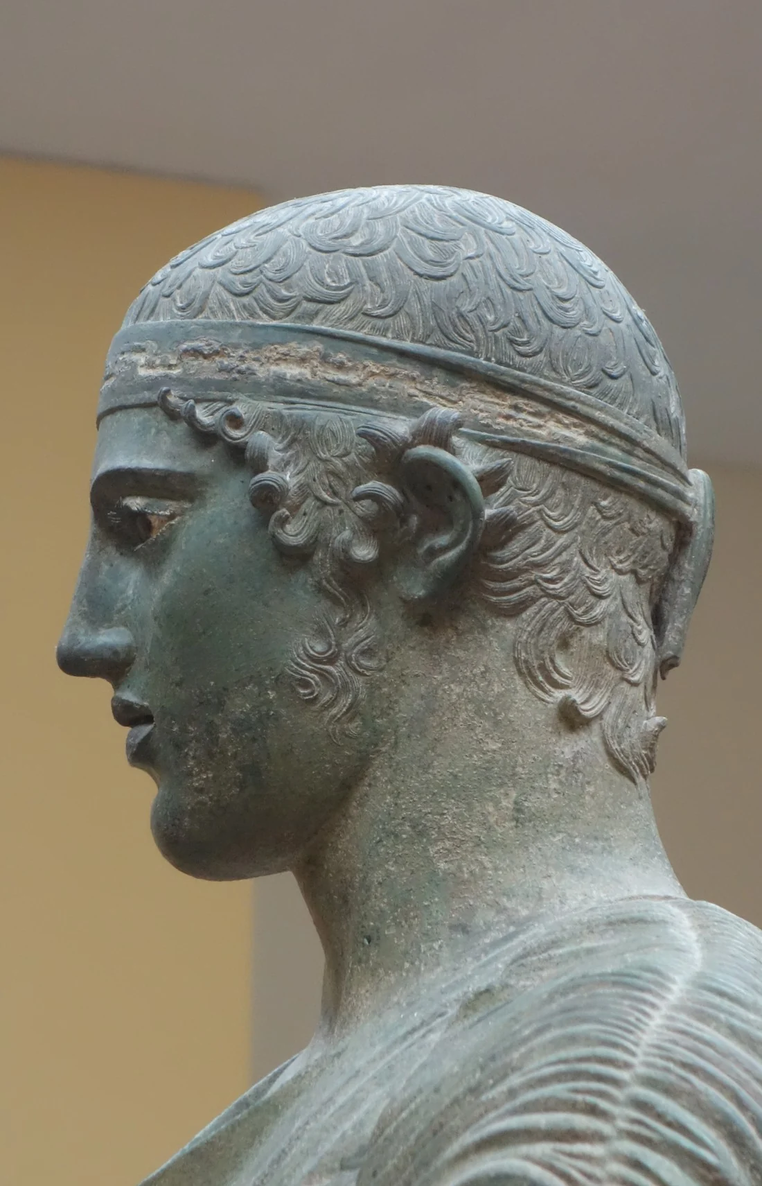 The bronze Charioteer of Delphi in profile, his inlaid eye still bright after 2,500 years