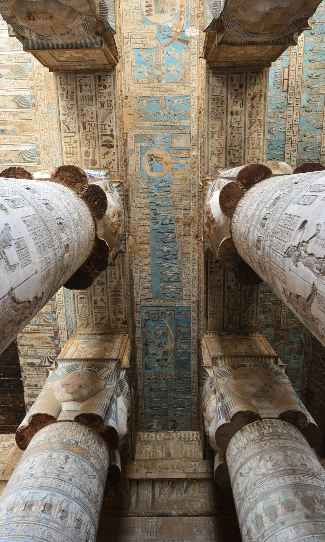 Looking up between the Hathor columns at the painted blue ceiling of the temple of Dendera